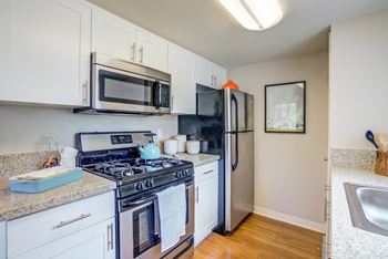 Model home kitchen with dishwasher, gas stove, refrigerator, granite countertops and hardwood inspired flooring.